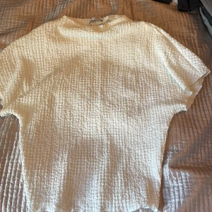 Vit strukturerad topp från Zara - Säljer en vit topp från Zara med strukturerat tyg och lös passform. Toppen har korta ärmar och rund halsringning, perfekt för en stilren och enkel look.