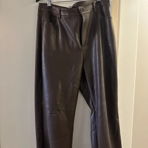 Bruna skinnbyxor från Bik Bok - Snygga bruna skinnbyxor från Bik Bok med normal passform. Byxorna har klassisk midja, raka ben och stängs med knapp och dragkedja. Perfekta för dig som vill ha en trendig look med lite edge.