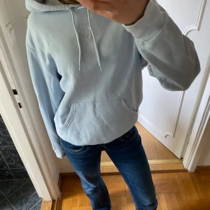 Ljusblå hoodie från monki - Säljer en ljusblå hoodie från monki med klassisk huva och magficka. Tröjan har långa ärmar och en avslappnad passform, perfekt för en chill vardagslook. Med ett gulligt litet tryck på framsidan 😊