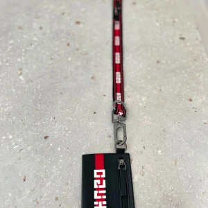 Hugo boss korthållare med band - Jag säljer min Hugo boss korthållare eftersom jag inte använder den längre. Finns lite skador på bandet som syns på bilden, men förutom det så är den i väldigt bra skick. Framsidan har en dragkedja för småsaker. Baksidan har tre platser för kort. 