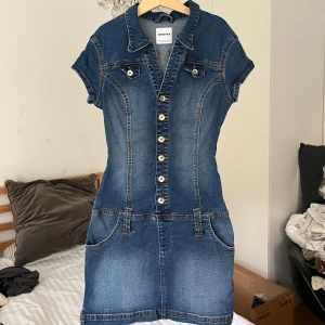 Jeansklänning Bershka - Jeansklänning från Bershka köpt i Spanien förra sommaren men knappt använd❣️Den sitter som en smäck och man kan själv knäppa/knäppa upp toppen så att den passar bättre, det finns ett skärp som man kan sätta på om så önskas 😊