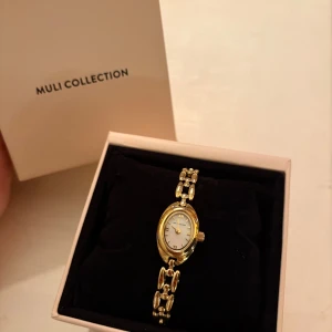 Guldfärgad klocka från Muli Collection - Helt NY ”oval heritage” klocka från Muli. Väldigt stilren och elegant, klockan är vattentät, väl fungerande batteri. Armbandet mäter 17,5 mm med en bredd på 8 mm, urtavlan är 15 mm. Justerbart upp till 20 mm längd och kan även justeras till en mindre storlek. 24k Guldplätering Nickelfri   Fick den i present men aldrig använd. Ligger ute på andra sidor! Nypris: 1899kr   Säljer den för 1600kr