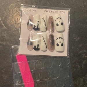 Halloween-inspirerade lösnaglar med svart och vitt motiv - Säljer ett set med lösnaglar i olika storlekar med Halloween-tema. Naglarna är dekorerade med svartvita motiv som stygn, ögon och droppar. Inkluderar självhäftande klisterlappar för enkel applicering.