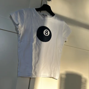 Vit t-shirt med 8-ball tryck från Subdued - Vit t-shirt från Subdued med ett stort svart 8-ball tryck på bröstet. Klassisk rund hals och korta ärmar. Perfekt för en avslappnad och cool stil.