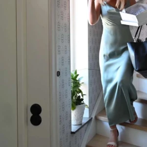 Satin långklänning  - Säljer en elegant ljusgrön långklänning med v-ringning och slits framtill. Klänningen har smala axelband och en figurnära passform som ger en stilren siluett. 