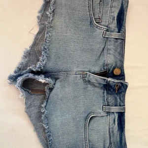 Ljusblå jeansshorts med fransar från Topshop Moto - Säljer ett par lågmidjade ljusblå jeansshorts från Topshop Moto. Shortsen har fransiga kanter, klassiska fickor fram och bak samt knapp och dragkedja. Perfekta för sommaren och har en snygg, avslappnad look. De är storlek 36 petite! Midjemåttet rakt över är 32 cm💞