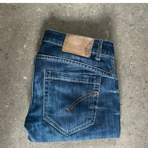 Blå jeansbyxor från Dondup - Säljer ett par klassiska blå jeansbyxor från dondup med snygga slitningar och kontrastsömmar. Byxorna har normal passform och raka ben, samt klassisk femficksdesign och läderpatch bak i midjan. Originalpris är 3000kr!