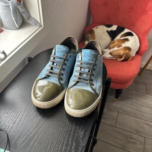 Blå sneakers från Lanvin - Säljer ett par snygga sneakers från Lanvin i ljusblått tyg med gröna detaljer på tå och häl. Perfekta för dig som vill sticka ut med stilrena men unika sneakers.