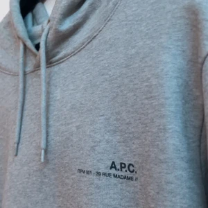 Grå hoodie från A.P.C. - Säljer en stilren grå hoodie från A.P.C. med diskret svart logga och text på bröstet. Tröjan har huva med dragsko och långa ärmar. Perfekt för en avslappnad look och passar till det mesta.