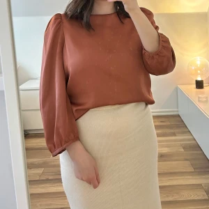 Blus från Mango - Säljer en blus med puffärmar och rund halsringning. Blusen har en elegant, slät yta och är tillverkad i ett lätt glansigt material som ger en lyxig känsla. Har en fläck (bild 4) som en steamer lämnat efter sig, syns dock inte när den är instoppad.