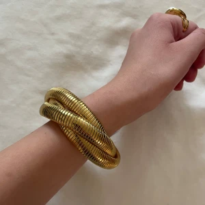 Guldfärgat spiralarmband - Aldrig använt! Säljer ett snyggt och chunky armband i guldfärgad metall med spiralformad design från Scandivv. Armbandet är flexibelt och perfekt för att snygga till en simpel outfit.