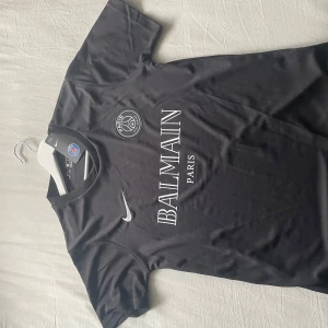 Svart PSG x Balmain fotbollströja från Nike - Säljer en svart PSG fotbollströja i samarbete med Balmain Paris. Tröjan är kortärmad och har Nike-logga samt PSG-emblem på bröstet. Tillverkad i Dri-FIT-material som andas och passar perfekt till träning eller match. Aldrig använd, passade inte