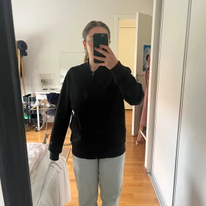 Svart mockajacka med dragkedja - Säljer en svart mockajacka med dragkedja framtill. Jackan har en enkel och stilren design med rund halsringning och långa ärmar. Perfekt för dig som gillar en clean look och vill ha något som funkar till många outfits.