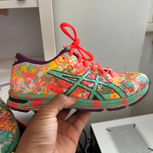 Färgglada Asics sneakers med mönster - Säljer ett par riktigt färgstarka Asics sneakers med unikt, färgstänkt mönster i orange, grönt, gult och rosa. Skorna har snörning och en bekväm, dämpad sula som passar perfekt för träning eller vardag. Ikoniska Asics-loggan på sidan. Prisen är inte huggen i sten så de bara komma med förslag