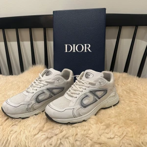 Vita Dior B30 sneakers med grå detaljer - Säljer mina vita dior B30, bara använda ett par gånger men som du kan se så har den 1 fläck på ena skon därav priset. Kommer med originalkartong och dustbag. 