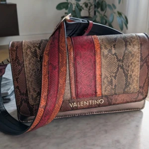 Axelväska från Valentino - Säljer en snygg axelväska från Valentino med ormskinnsmönster i bruna, röda och beige toner. Väskan har bred axelrem, guldfärgad logga och dragkedja inuti. 
