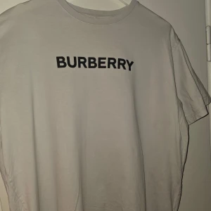 Vit t-shirt från Burberry - Säljer en vit t-shirt från Burberry med klassisk svart logotyp på bröstet. T-shirten har rund halsringning och är tillverkad i mjuk bomull. Perfekt för en clean och stilren look.