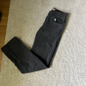 Grå jeansbyxor Levis 551Z Authentic Straight - Säljer ett par grå Levis 551Z Authentic Straight jeans med klassisk femficksdesign och raka ben. Byxorna har normal passform och är tillverkade i jeanstyg. Perfekta för dig som gillar en tidlös stil med raka linjer. Det är barnstorlek 14A. Motsvara XL i barnstorlek. 