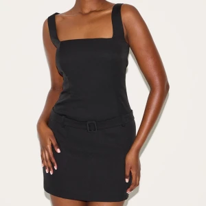 Svart kortklänning med bälte från PLT  - Svart miniklänning med breda axelband och fyrkantig ringning. Klänningen har ett bälte i midjan och dragkedja i ryggen. Helt ny med prislapparna kvar. Storlek UK 12, men liten i storlek så passar S-M. 