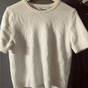 Vit kortärmad stickad tröja - Säljer en enkel och stilren vit stickad tröja med korta ärmar och rund halsringning. Tröjan har en något croppad passform och är perfekt för en avslappnad look