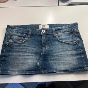 Mini Jeanskjol med Låg midja  - Säljer en lågmidjad blå jeanskjol från BDG Urban Outfitters. Kjolen är i minilängd med femficksdesign, knapp och dragkedja framtill. Såå snygg detalj på bakfickan! Hör av dig vid intresse eller frågor💕💕