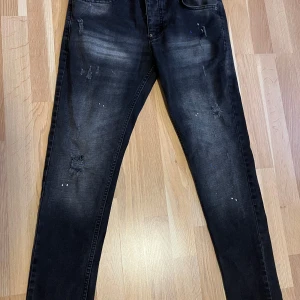 Svarta skinny jeans från Dsquared2 - Säljer ett par svarta skinny jeans från Dsquared2 med slitningar och små färgstänk framtill. Jeansen har klassisk femficksdesign och smal passform.  Strl 42 . ( motsvarar strl S) . Nyskick !
