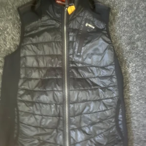 Svart dunväst från Parajumpers - Snygg svart dunväst från Parajumpers med quiltad framsida och dragkedja hela vägen. Västen har en bröstficka med dragkedja och diskret logga i nacken. Perfekt lager-på-lager-plagg med sportig vibe och stilren look.