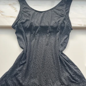 Svart leopardmönstrad linnetopp  - Snygg svart linnetopp med diskret leopardmönster. Toppen är ärmlös och kan bäras på båda hållen. Antingen som en urringad topp eller baklös topp. Den är lite genomskinlig men man behöver ingen undertröja. Vet inte vilket märke då jag klippt av märket men storleken är M/S. 