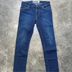 Jacob Cohen blå skinny jeans - Snygga blå skinny jeans från Jacob Cohen, tillverkade i Italien. Klassisk femficksmodell med bruna kontrastsömmar, läderpatch bak och diskret broderad logga på myntfickan. Jeansen har knappgylf och är gjorda i stretchig bomull för en tight passform.
