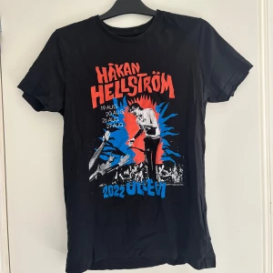 Håkan Hellström Ullevi 2022 t-shirt - Svart t-shirt med färgstarkt tryck från Håkan Hellströms Ullevi-konserter 2022. Framsidan har röd och blå grafik med konsertdatum och en bild på Håkan på scen. Klassisk passform och rund hals, perfekt för fans som vill sticka ut.