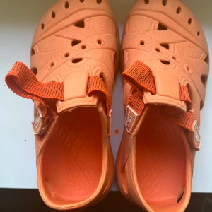 Orange strand sandaler från O'Neill - Coola orange strand sandaler från O'Neill med sportig design och breda remmar. Skorna har ventilerande hål, justerbara spännen och en rejäl, mönstrad sula i syntetmaterial. Perfekta för sommardagar och strandhäng. Mjuka och sköna.