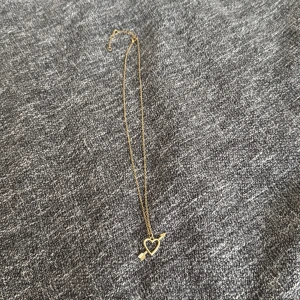 Guldigt halsband med hjärthänge - Snyggt halsband i guld med ett hjärthänge som har en pil genom sig. 