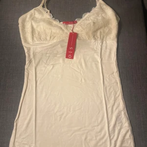 Vit spetslinne OIS - Supersöt vitspetstopp från OIS med tunna axelband och v-ringning. Överdelen har fina spetsdetaljer stor i storlek