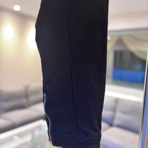 Svarta byxor  - Svarta byxor med smal passform och coola dragkedjor både baktill och vid bensluten. Byxorna har en stilren look och är tillverkade i ett stretchigt material som sitter snyggt. Den har också ”vikta” detaljer som går lodrätt på benen. Oanvänd utan prislapp.