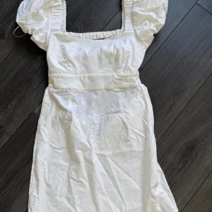 Vit kortklänning med puffärmar - Superfin vit kortklänning från Stradivarius med puffiga kortärmar och fyrkantig ringning. Klänningen har markerad midja, dragkedja i sidan och är gjord i bomull. Perfekt för sommarens alla tillfällen och ger en romantisk vibe.