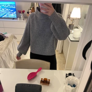 Grå stickad tröja med ballongärm - Mysig grå stickad tröja med ballongärmar. Tröjan är lite croppad och har en hög krage som ger en chill vibe. Perfekt att slänga på sig när det är kallt ute.
