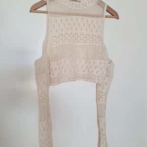 Beige stickad bolerotopp från Zara - Supersöt beige/offwhite stickad bolerotopp från Zara med genombrutet mönster och långa ärmar. Toppen har olika stickade strukturer och är croppad med öppen front och off shoulder ärmar.