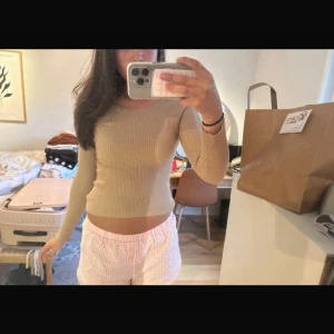 Beige ribbad långärmad topp med snörning - Säljer en beige ribbad långärmad topp med snygg snörningsdetalj längs ena ärmen. Toppen är croppad och har en tight passform som framhäver figuren. Perfekt för dig som gillar unika detaljer och vill sticka ut lite extra.