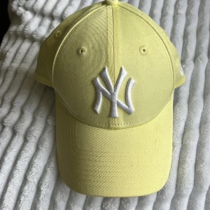 Gul New Era Yankees keps 9FORTY - Snygg gul New Era 9FORTY keps med vit broderad New York Yankees-logga framtill. Klassisk böjd skärm och justerbar passform. Tillverkad i bomull, perfekt för att lyfta din streetstyle.