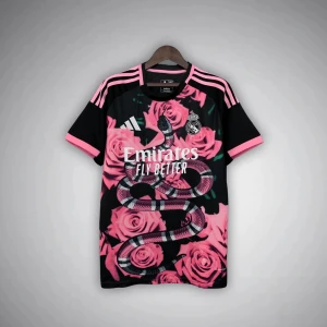 Real Madrid x Adidas rosa/svart fotbollströja - Unik Real Madrid fotbollströja från Adidas med svart bas, rosa rosor och en stor orm på framsidan. Tröjan har korta ärmar med rosa detaljer och klassiska Adidas-ränder på axlarna. Broderad Real Madrid-logga på bröstet. Tillverkad i ventilerande funktionsmaterial.