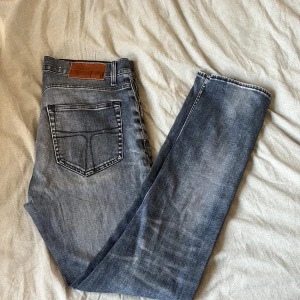 Tiger Of Sweden jeans  - Snygga blå jeans från T/J med klassisk femficksdesign och raka ben med ett ny pris på 1599kr. Jeansen har en mellanblå tvätt med slitningar och kontrastsömmar. Skinnpatch med T/J-logga bak i midjan. Perfekta för en avslappnad och stilren look. Sitter även perfekt vid midjan och anklarna. 