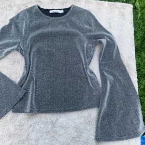 Glittrig silvertröja från NA-KD - Supersnygg glittrig silvertröja från NA-KD i storlek XS. Tröjan har långärmade utsvängda ärmar och är gjord i ett stretchigt, glittrigt material som verkligen sticker ut. Perfekt för dig som vill ha något extra till outfiten!