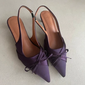 Lila kitten heels  - Snygga lila pumps  med spetsig tå, låg klack och söt rosett framtill! Skorna har öppen häl med smal rem och är tillverkade i satinliknande material🩷 Aldrig använda pga för stora