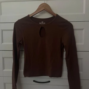 Brun långärmad topp från Hollister - Säljer en brun långärmad topp från Hollister Must-Have Collection. Toppen har en rund halsringning och en snygg droppformad cut-out framtill. Mjuk och stretchig bomullskänsla, perfekt till jeans eller kjol för en chill look.