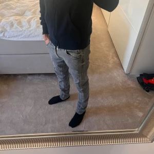 Grå jeans från Lee - Säljer ett par grå skinny jeans från Lee med klassisk femficksdesign och dragkedjegylf. Jeansen har en smal passform och är tillverkade i mjukt denimtyg som sitter snyggt på benen. Perfekta för dig som gillar en stilren och modern look. Storlek 30/32