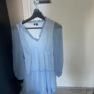 Ljusblå kortklänning med volang - Supersöt ljusblå kortklänning från veromoda med små vita prickar, v-ringning med volangkant och långa, transparenta ärmar.  . 