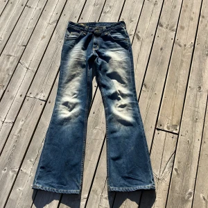 Blå bootcut jeans från Lee - Säljer ett par blå bootcut jeans från Lee i 100% bomull. Jeansen har tydliga slitningar och ljusa partier framtill och baktill för en cool vintagekänsla. Klassisk femficksmodell med normal passform och breda benslut. Perfekta för dig som gillar retrostil. Men skriv något om du funderar över.💕💕💕
