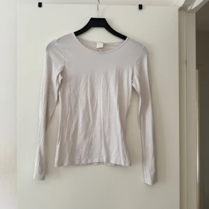 Vit långärmad basictröja H&M  - Enkel och stilren vit långärmad tröja från H&M Basics i storlek S. Tröjan har rund halsringning och är gjord i mjuk bomull, perfekt att ha som basplagg. Sitter tajt mot kroppen och passar till allt.