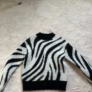Zebramönstrad stickad tröja - Snygg stickad tröja med svartvitt zebramönster. Tröjan har rund halsringning, långa ärmar och ribbade muddar vid ärmslut och nederkant. Perfekt för dig som vill sticka ut med en cool och trendig look.