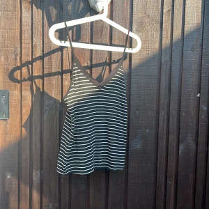 Svartvitrandig linnetopp med smala band - Säljer en svartvitrandig linnetopp med smala axelband och v-ringning. Toppen har tunna vita horisontella ränder och svart kant runt halsen. Perfekt för varma dagar och enkel att matcha med jeans eller kjol.